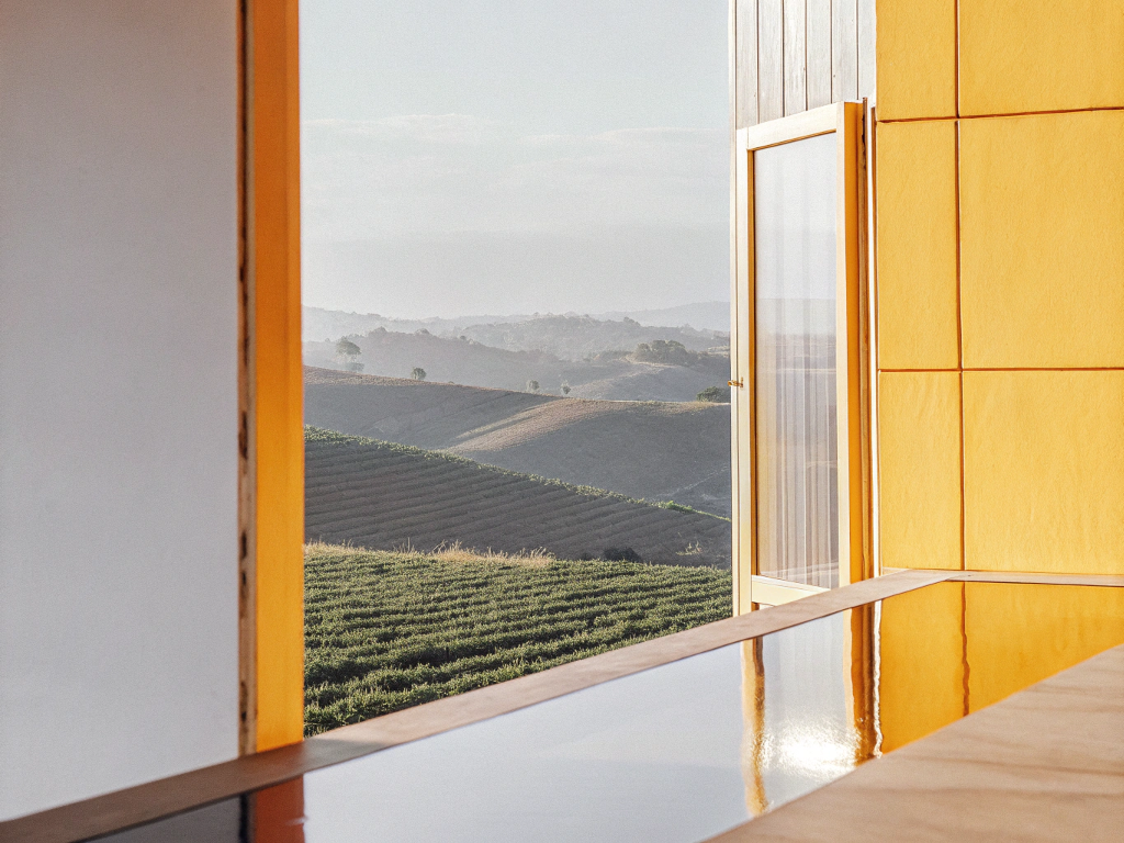 View from a modern building with a water feature, overlooking hazy coffee hills in Campo das Vertentes.