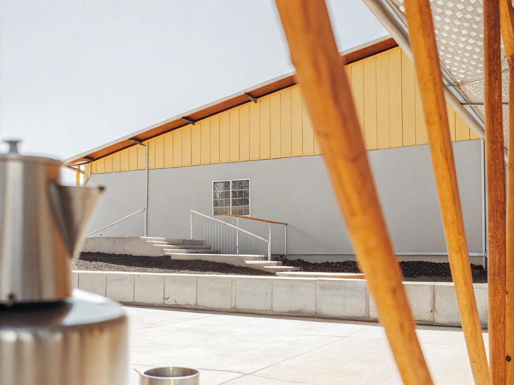 Modern farm building with yellow accents in Jequitinhonha, viewed through wooden poles.