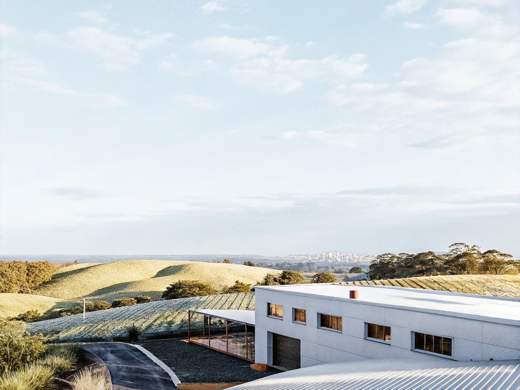 A modern farm building set against rolling hills of coffee with the city in the distance.
